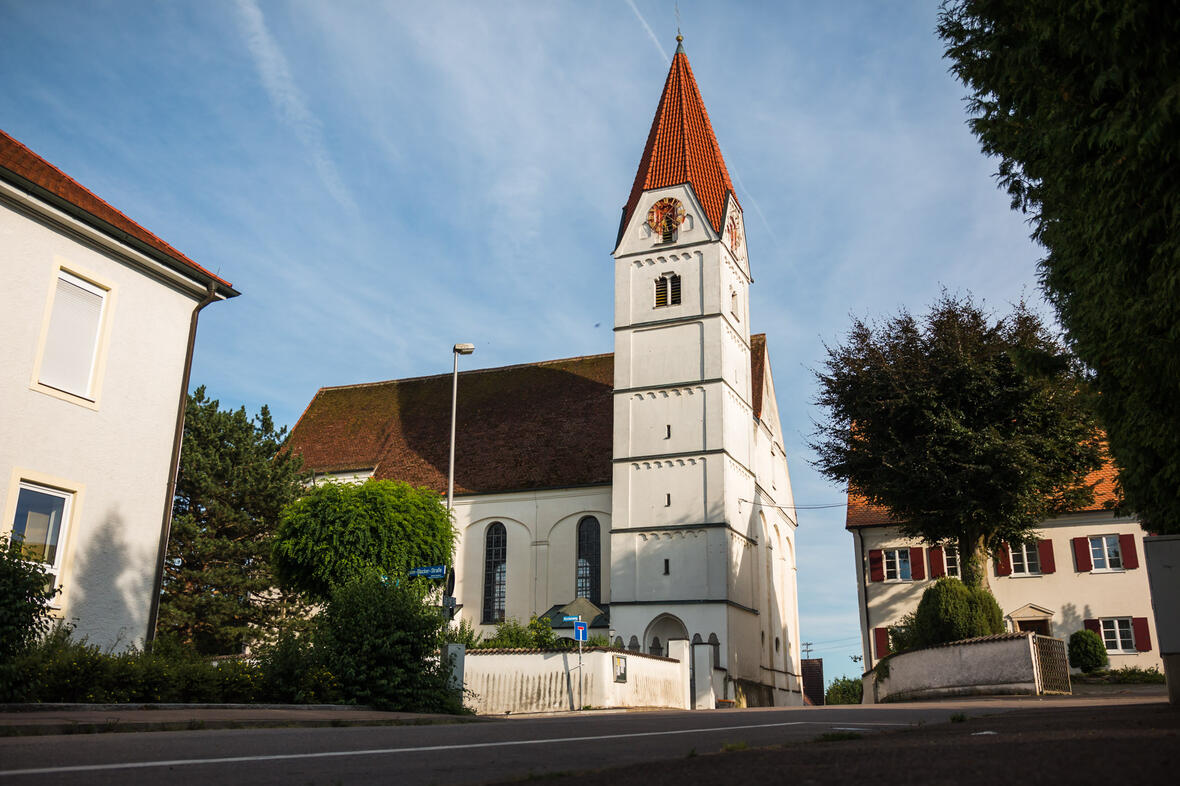 Kirche in einem Ort mit historischem Charme, umgeben von Bäumen und Wohnhäusern.