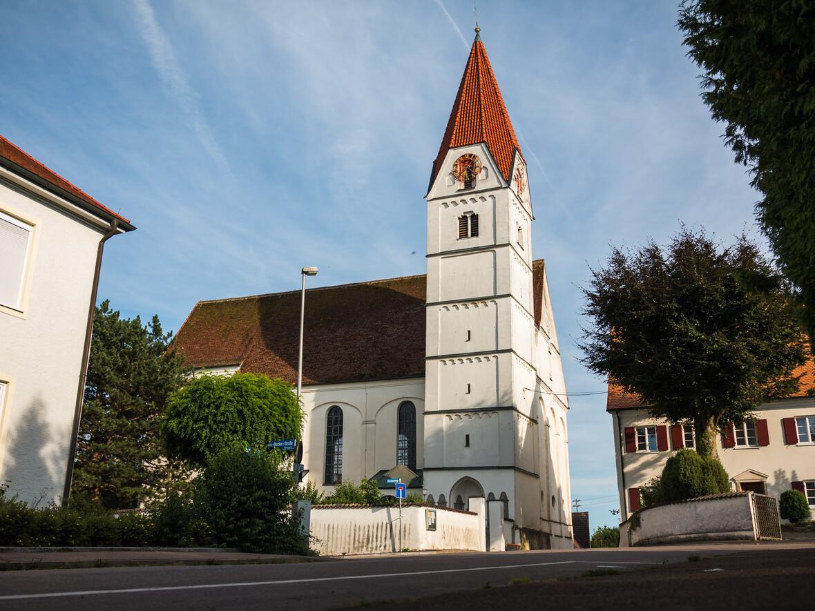 Kirche in einem Ort mit historischem Charme, umgeben von Bäumen und Wohnhäusern.